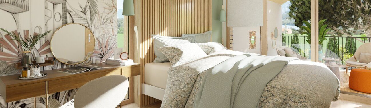 A cozy, sunlit bedroom with a patterned bed, green throw, wooden vanity, and balcony view.