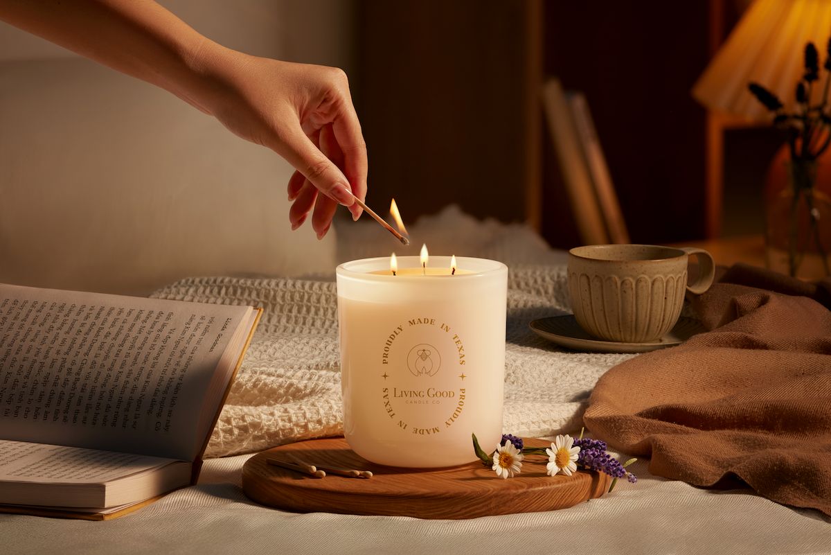 Living Good Candle Co. 15 oz three-wick beeswax candle being lit beside a book and tea in a cozy evening wind-down setting.