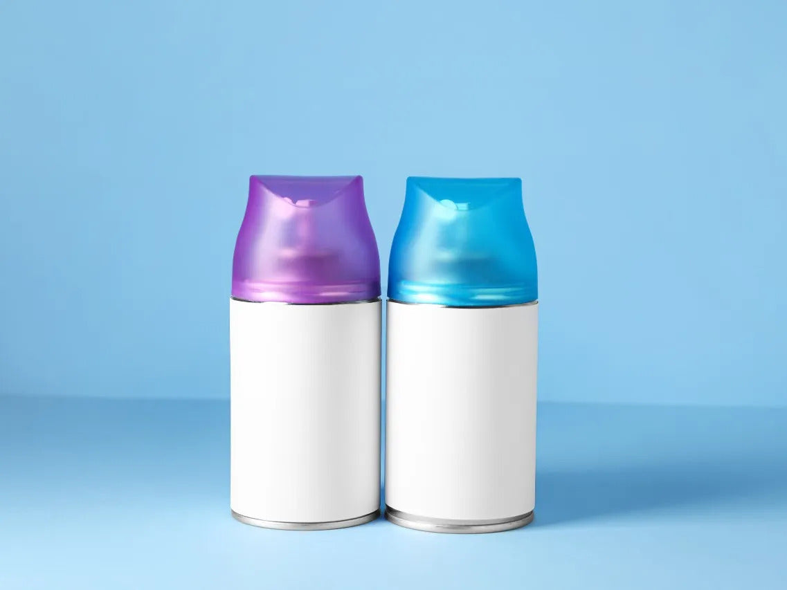 Two aerosol air freshener cans with blank white labels, one with a purple cap and the other with a blue cap, placed side by side against a light blue background.