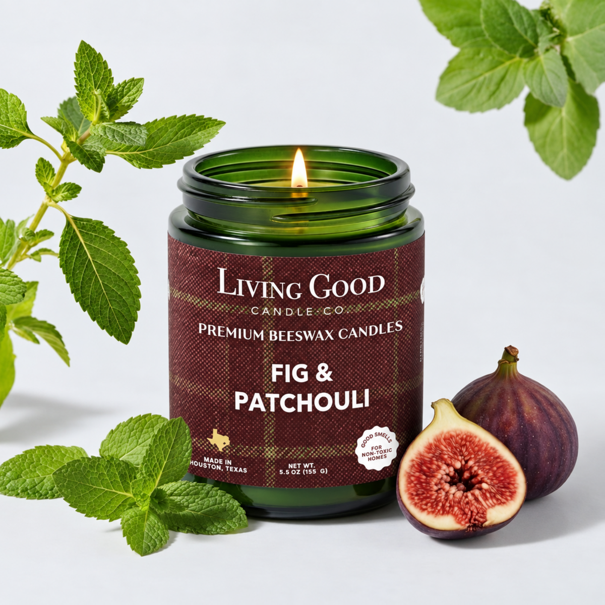 Fig & Patchouli 5.5 oz beeswax candle burning in a green glass jar beside fresh figs and green botanicals.