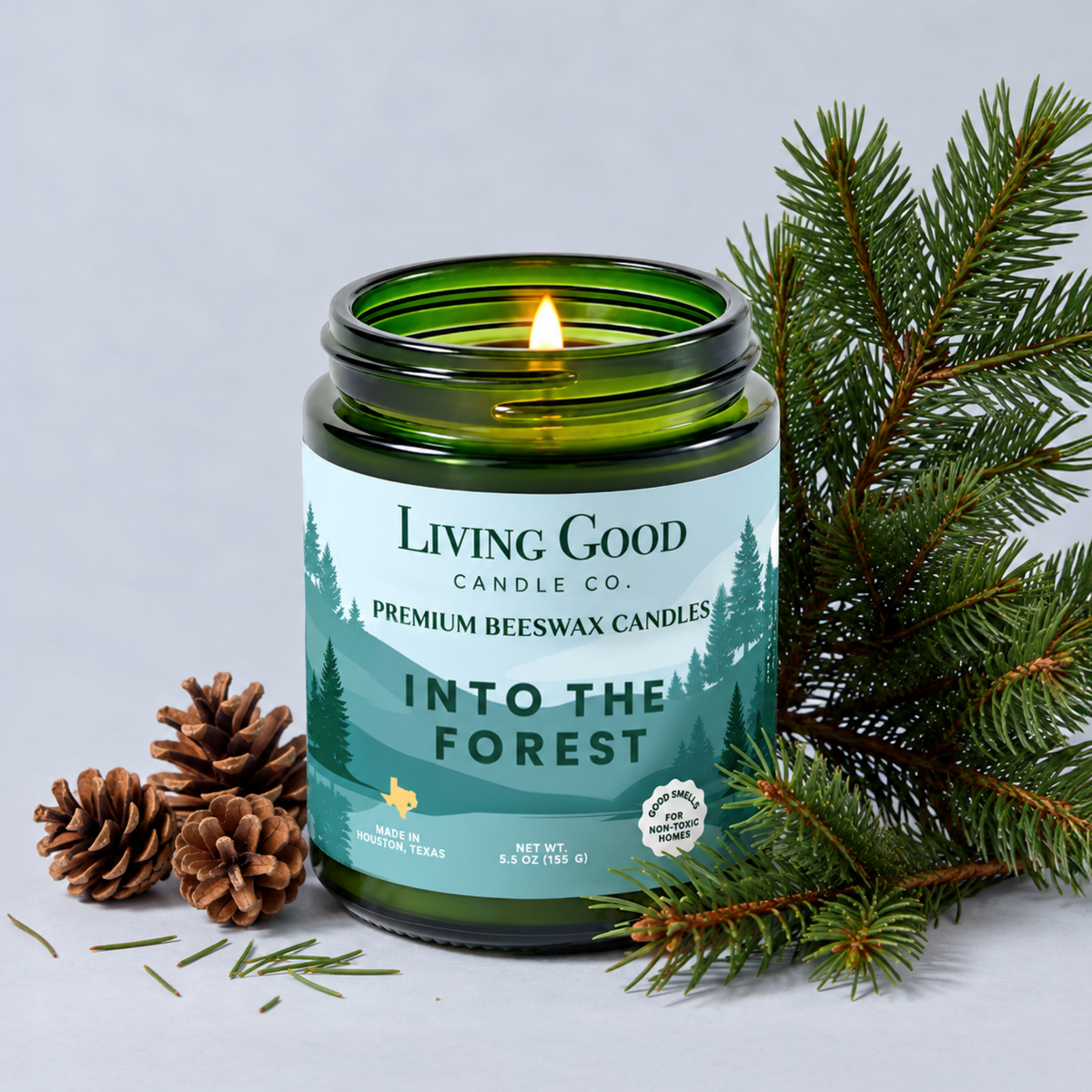 Into the Forest 5.5 oz beeswax candle by Living Good Candle Co. displayed with evergreen branches and pine cones.