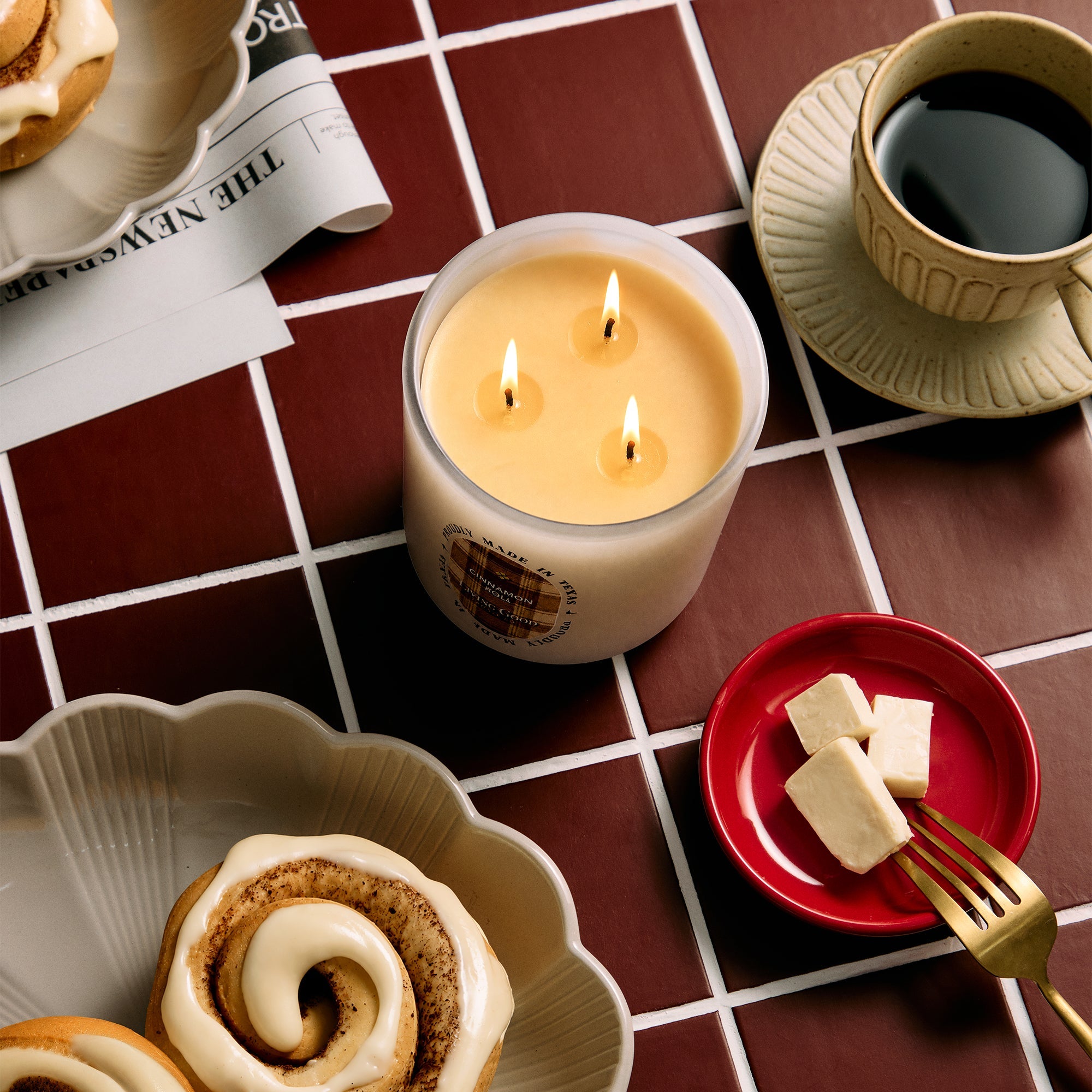 Cinnamon Roll candle flat lay with cinnamon rolls, coffee, and butter on a diner-style tile counter