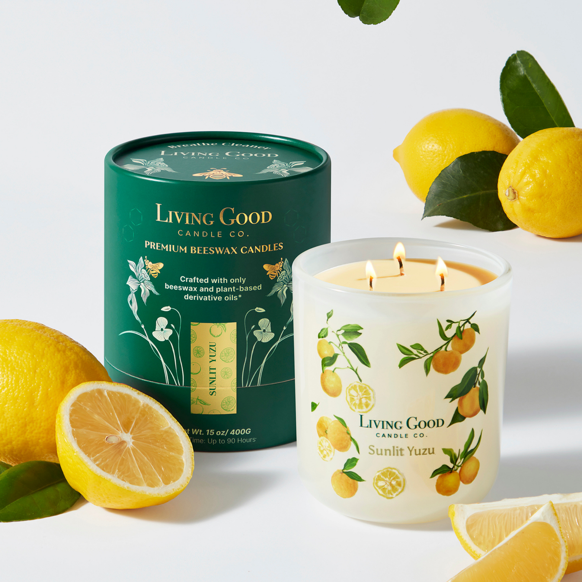 Living Good Candle Co. Sunlit Yuzu 15 oz three-wick beeswax candle burning beside fresh yuzu citrus and lemon.