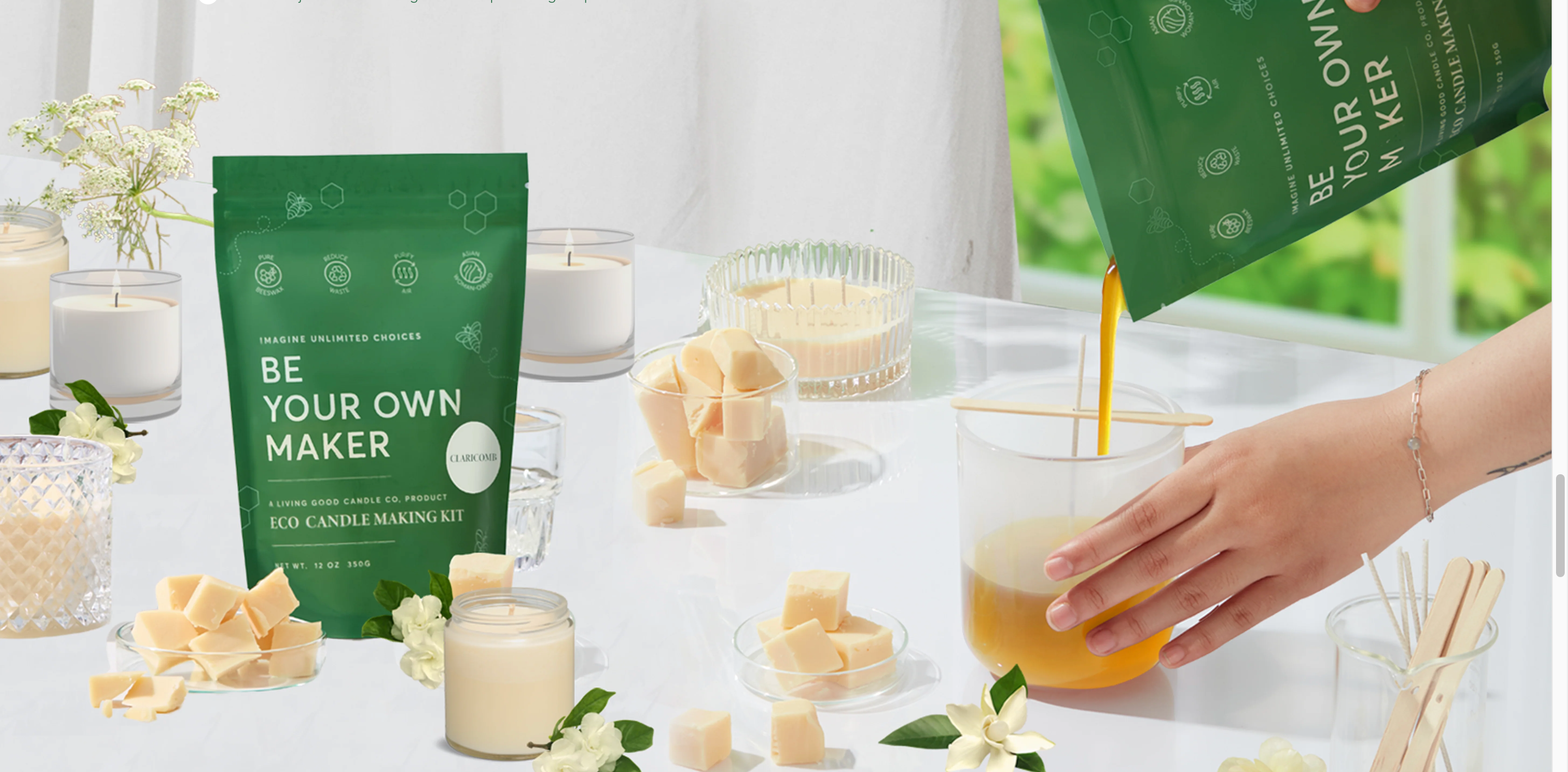 A hand pours melted beeswax into a candle mold from the Living Good Candle Co. Eco Candle Making Kit, surrounded by finished candles, wax cubes, and floral decor on a sunlit table with a green “Be Your Own Maker” pouch prominently displayed.