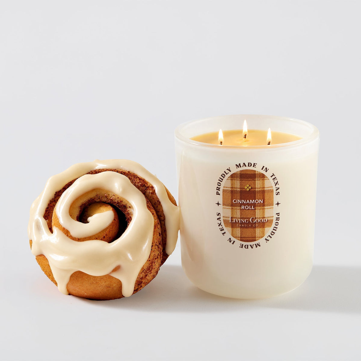 Living Good Candle Co. Cinnamon Roll beeswax candle beside an iced cinnamon roll on a clean white background.