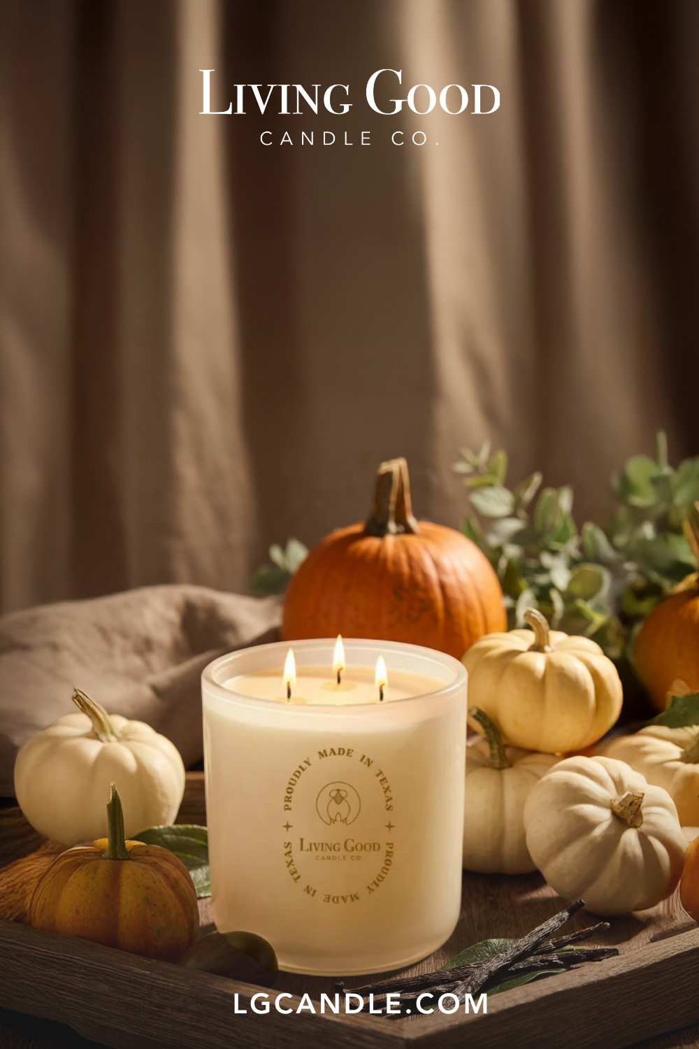 Living Good Candle Co. natural beeswax candle with three lit wicks surrounded by pumpkins in a warm autumn setting.