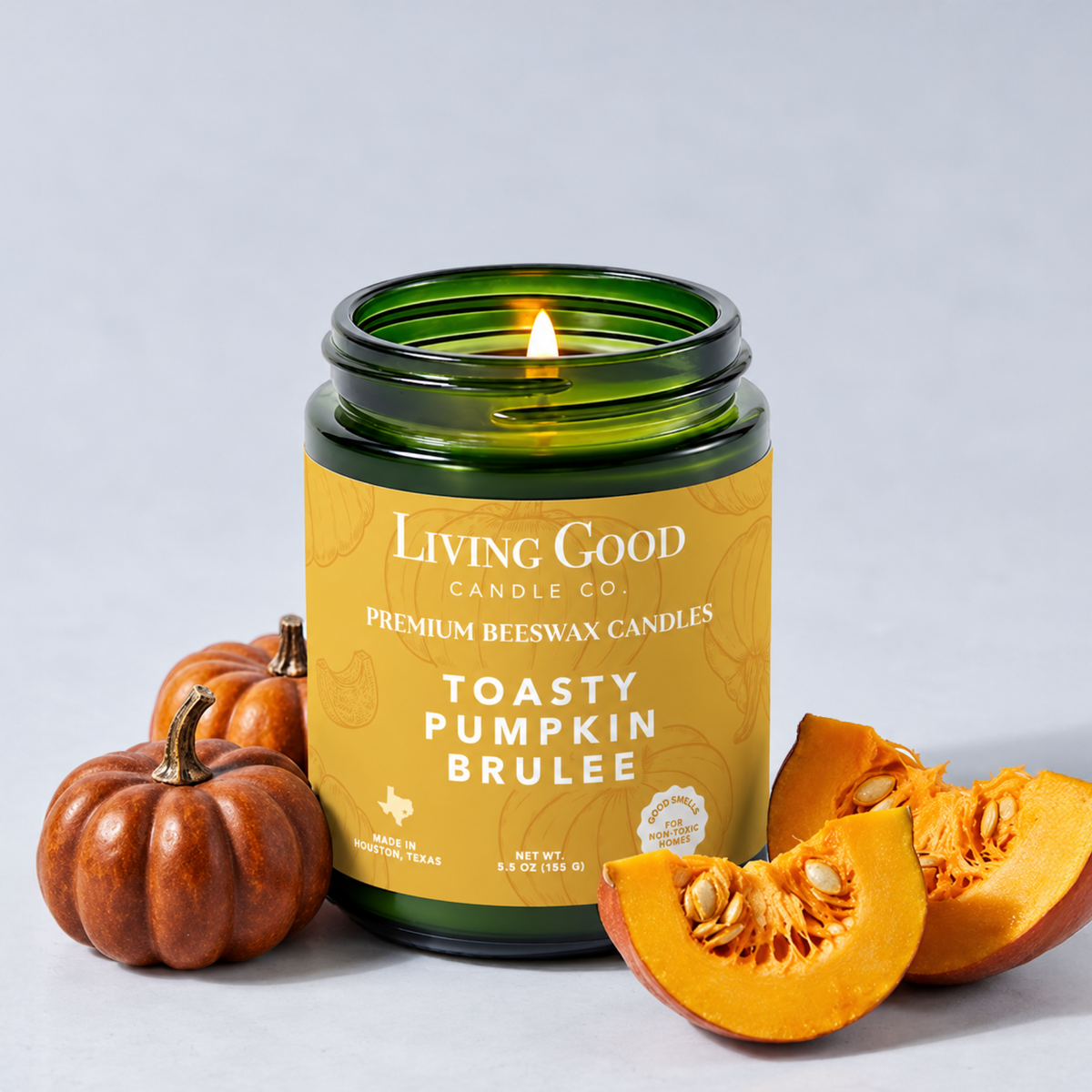Toasty Pumpkin Brulee 5.5 oz beeswax candle burning in a green glass jar beside fresh pumpkin.