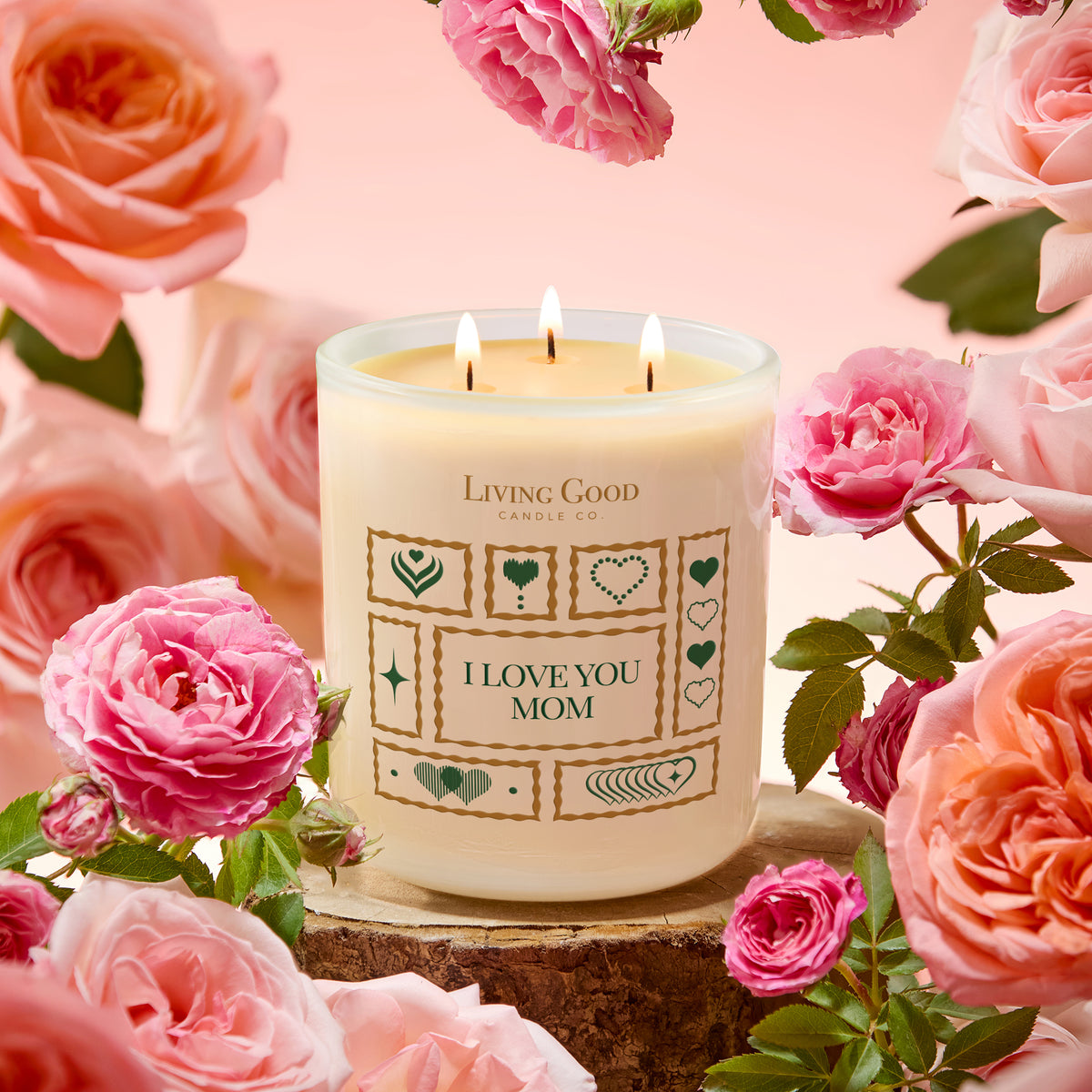I Love You Mom Mother’s Day beeswax candle surrounded by pink and peach roses with three lit cotton wicks.