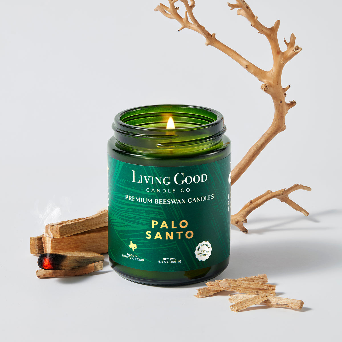 5.5 oz Palo Santo beeswax candle burning beside Palo Santo wood in a green glass jar by Living Good Candle Co.