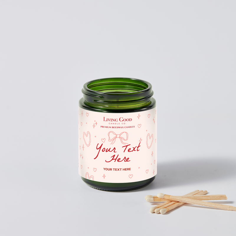 Personalized beeswax candle with a custom message label featuring pink hearts, bows, and red script on a green glass jar.