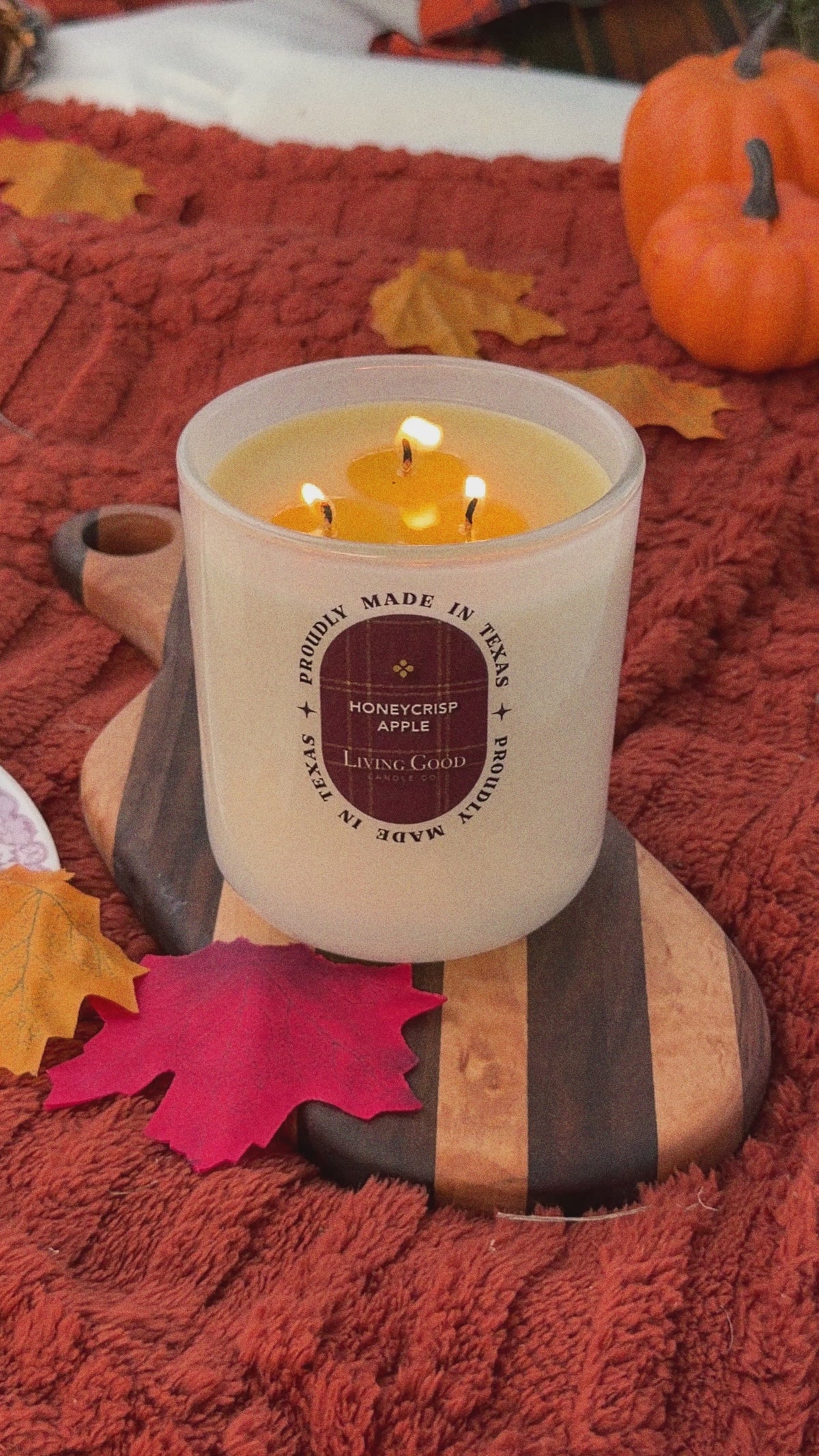 Living Good Candle Co. Honeycrisp Apple 15 oz three-wick beeswax candle burning in a cozy fall setting with autumn leaves and pumpkins.
