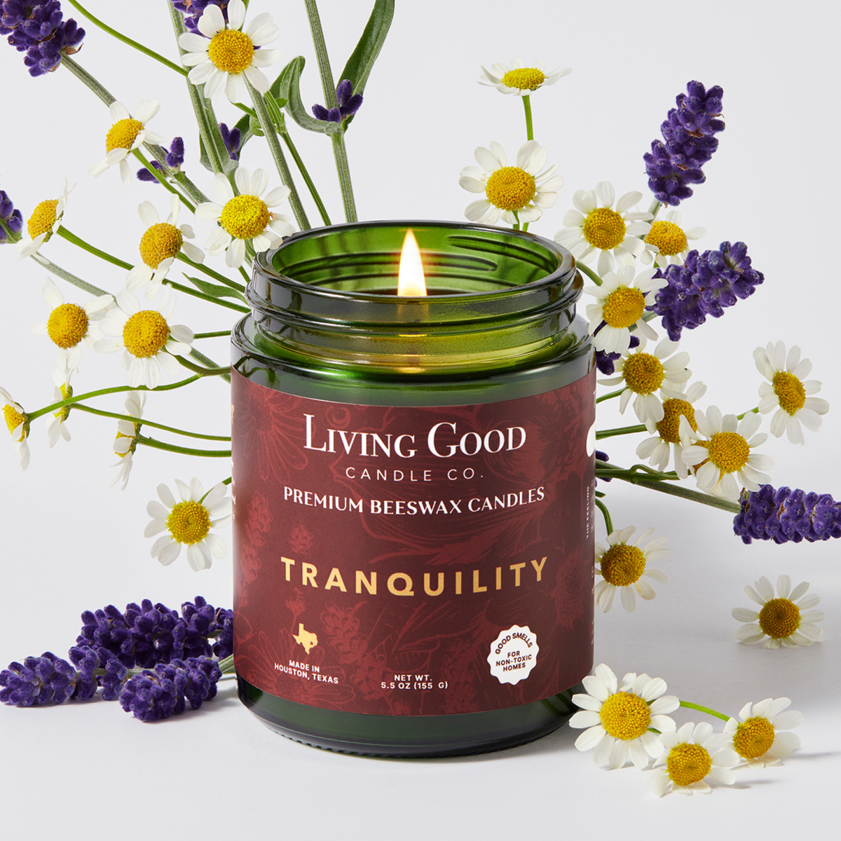 Tranquility 5.5 oz beeswax candle with a lit wick surrounded by lavender and chamomile flowers